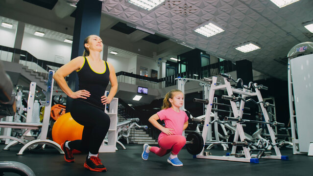 Mother and daughter in the gym, family performs physical doing exercises fitness, healthy lifestyle. Happy sports family training concept. Woman with her child doing stretching warm-up in the gym