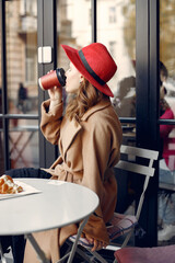 Girl with red hat sitting in a cafe outdoors and drinking coffee