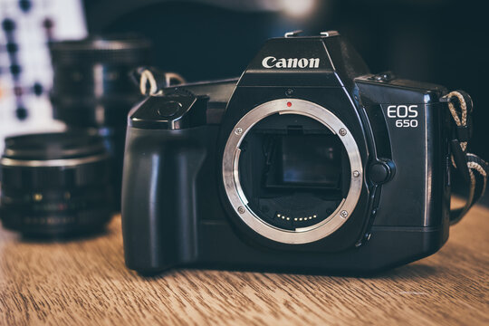 Old Japanese film camera on wooden table. Model Canon EOS 650, the first ever SLR with auto focus system. Front view, close up, vibrant tone.