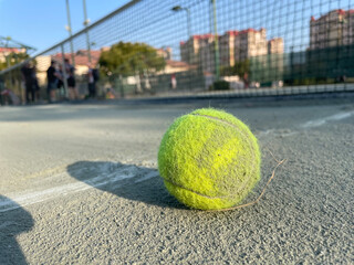 A closeup view of a tennis ball on a gray clay court with a clay court surface in the foreground