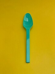 Plastic spoon with torquoise color on yellow background