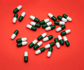 Pile of green and white capsules drugs on red background