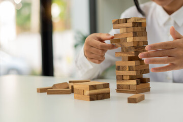 female hand gradually Pull wooden blocks from stacked unstable Jenga blocks to practice court tactics and tactics. Strategic Thinking and Risk