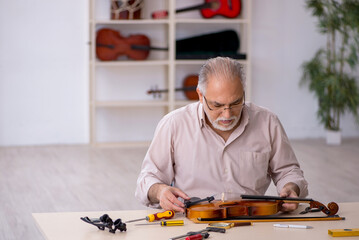 Old male repairman repairing musical instruments at workshop