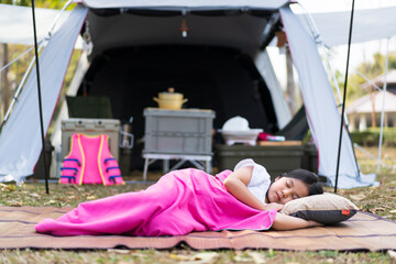 Asian child cute or kid girl camper sleeping on mat and grass lawn on nature camping tent or white cabin camp and comfortable in summer forest campground on holiday relax and family vacation travel