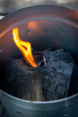 encendedor de  carb&oacute;n met&aacute;lico.
carb&oacute;n encendido .
flama.
manos acomodando carb&oacute;n.
carb&oacute;n vegetal. 