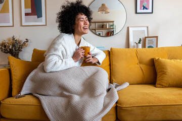 Happy African american woman enjoying quiet time at home laughing, drinking morning coffee sitting...