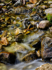 Naklejka na ściany i meble Small stones in a flowing stream with blurred water