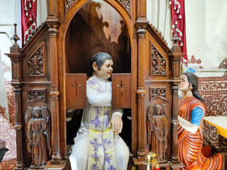 GOA, INDIA - 13 Jan 2022 Statue of priest sitting behind the grid and listening the confession in the church.Selective focus.