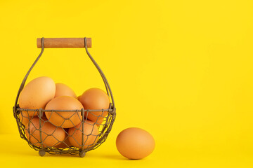 brown fresh farm eggs in a basket for festive easter on yellow background copy space for frontal...