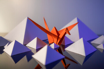 Orange origami swan in white paper pyramids 