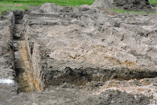 The deep excavation made for pouring concrete footing for a new house, two batter-boards and a red brick line