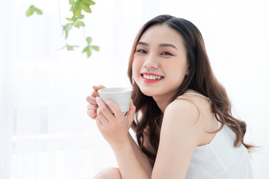 Image of beautiful young Asian woman drinking tea at home in the morning