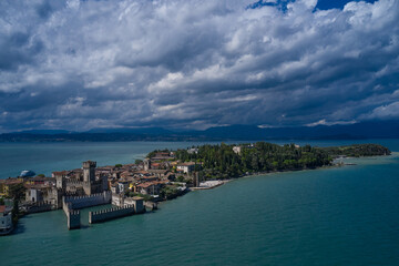 Naklejka na ściany i meble Rocca Scaligera Castle in Sirmione. Cumulus clouds over the island of Sirmione. Aerial view on Sirmione sul Garda. Italy, Lombardy. Panoramic view at high altitude. Aerial photography with drone.