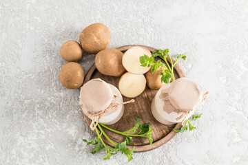 top view of two glass bottles with vegetable potato milk and chopped potato tubers on a wooden tray. gray concrete background.