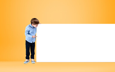 Preschool kid point at mockup poster on bright background