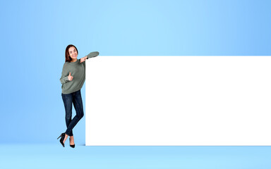 Woman shows thumb up near mockup poster on light background