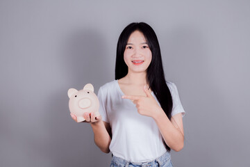 Lovely woman with long dark hair holding piggybank on gray background