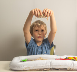 a boy with blond hair enthusiastically plays with sand in an inflatable sandbox for the house .