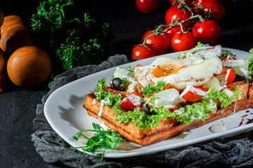 Waffle with fried egg and vegetables on dark background. Delicious traditional breakfast idea. Viennese waffles, belgian waffle recipe