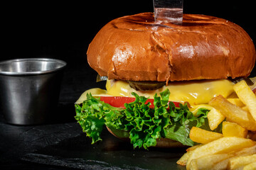 Delicious big burger with french fries on dark background