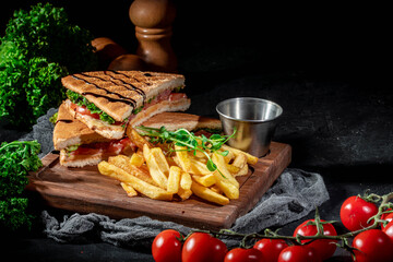 Sandwiches with ham, cheese, tomatoes and salad with toasted bread. Delicious sandwiches with french fries on dark background
