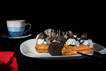 Plate of belgian waffles with ice cream, cookies and chocolate sauce on dark background