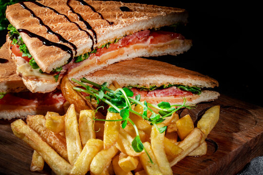 Sandwiches with ham, cheese, tomatoes and salad with toasted bread. Delicious sandwiches with french fries on dark background