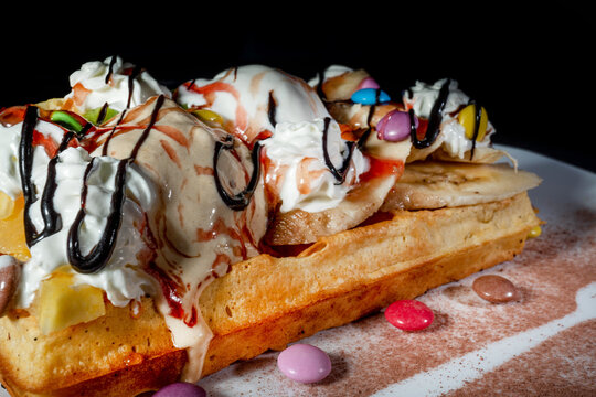 Plate of belgian waffles with ice cream, caramel sauce and fresh berries on dark background