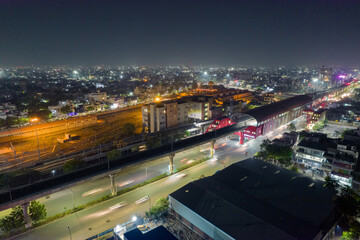 elevated metro track station with train leaving and light trails over lit busy street and yard in...