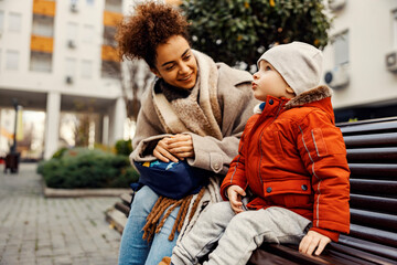 A cute little boy sitting outside with a young woman, nanny or caregiver, and telling something important. - obrazy, fototapety, plakaty