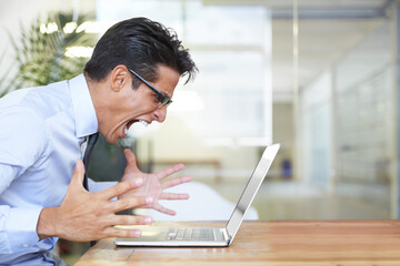 When your computer crashes. Profile of an angry businessman shouting at his laptop at work.