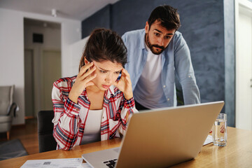 Woman with headache paying bills online with her husband.