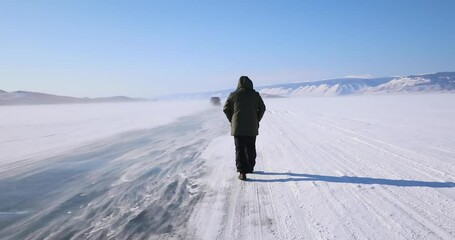 A man walks on the frozen lake Baikal - Snow is flying over surface of ice. Snowflakes fly on ice of Lake Baikal - Powered by Adobe