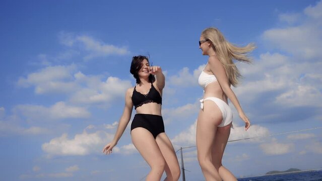 Smiling two attractive young women in bikini dancing and enjoying a summer holiday party in cruise yacht on sea and blue sky background