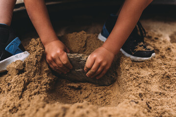 Kleiner Junge spielt im Sand mit einem Stein in seinen Händen horizontal