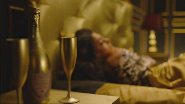 Side view of beautiful sexy woman laying on luxury bed with golden color satin linens . Caressing , touching her body . Portrait of girl lies and looking at camera . Hotel room . Slow motion close up 