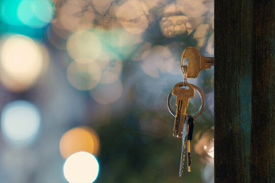 The keys with keyring in the door keyhole with blurred night lights background, selective focus