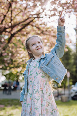 Little redhead girl points uphill on a background of sakura in the garden.