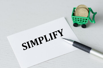 SIMPLIFY text on card on the table next to the pen and coins in the basket