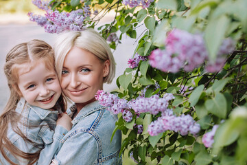 Fototapeta premium Portrait of mother and daughter close up on a lilac background. Young mother with baby having fun in the park near lilac.