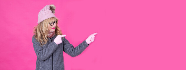 woman in winter clothes, sweater, hat, gloves and scarf pointing or showing with copy space