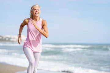 Keuken spatwand met foto Mature woman running along the shore of the beach. Older female doing sport to keep fit © javiindy