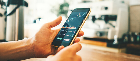 Woman's hands in coffee shop with mobile investing app in her hand, close-up