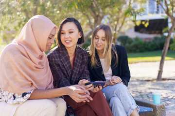 Smiling young diverse girls watching video on smartphone in park
