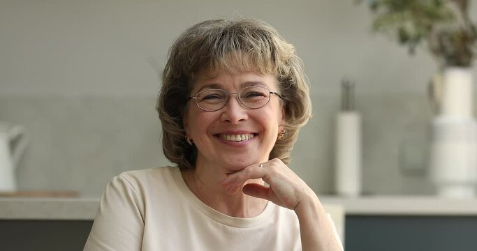 Head shot portrait attractive mature woman smile look at cam. Older female wear spectacles staring at camera rest alone at home, enjoy carefree retired comfort life. Eyesight check up services concept