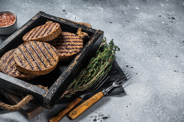 Roasted meat free patties, plant based meat burger cutlets in wooden tray with herbs. Gray background. Top view. Copy space