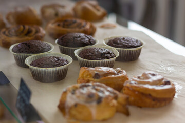 Variety baked muffins and buns in glass showcase at bakery cafe.