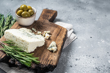 Danish blue cheese on a wooden board with olives and rosemary. Gray background. Top view. Copy space