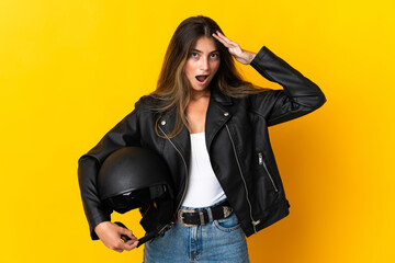 Woman holding a motorcycle helmet isolated on yellow background with surprise expression